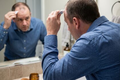 Homme d'âge moyen appliquant un traitement capillaire devant un miroir