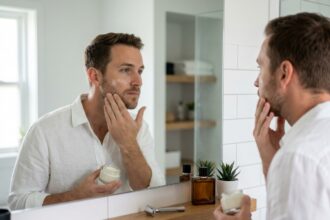 Homme prenant soin de sa peau avec une crème hydratante dans une salle de bain moderne et épurée